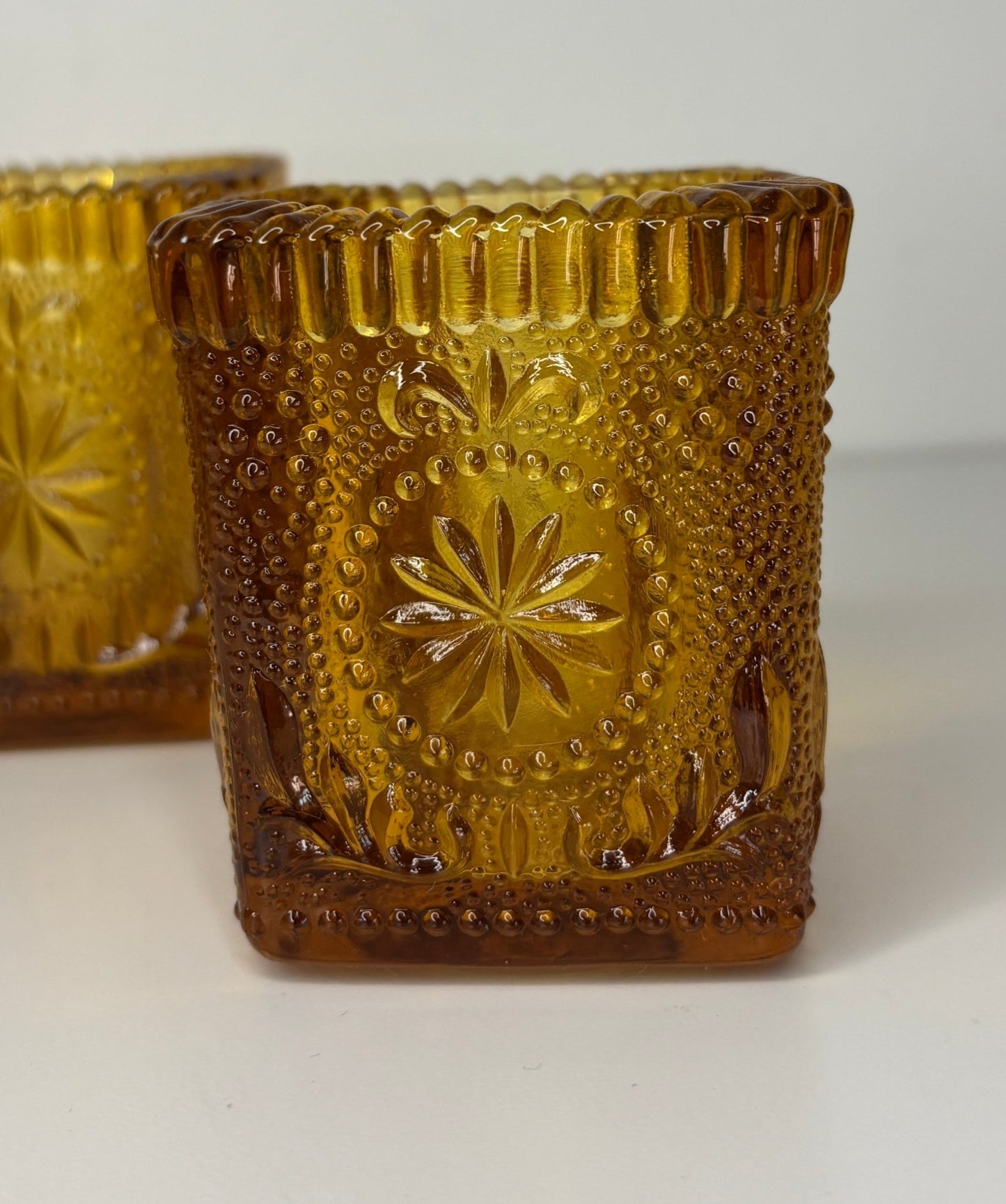 Decorative amber glass candle holders with embossed designs on a white background