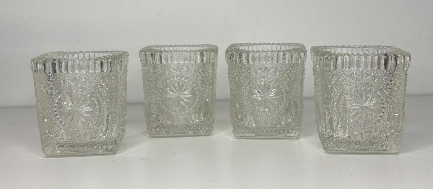 Four clear glass candle holders with textured design on a white background