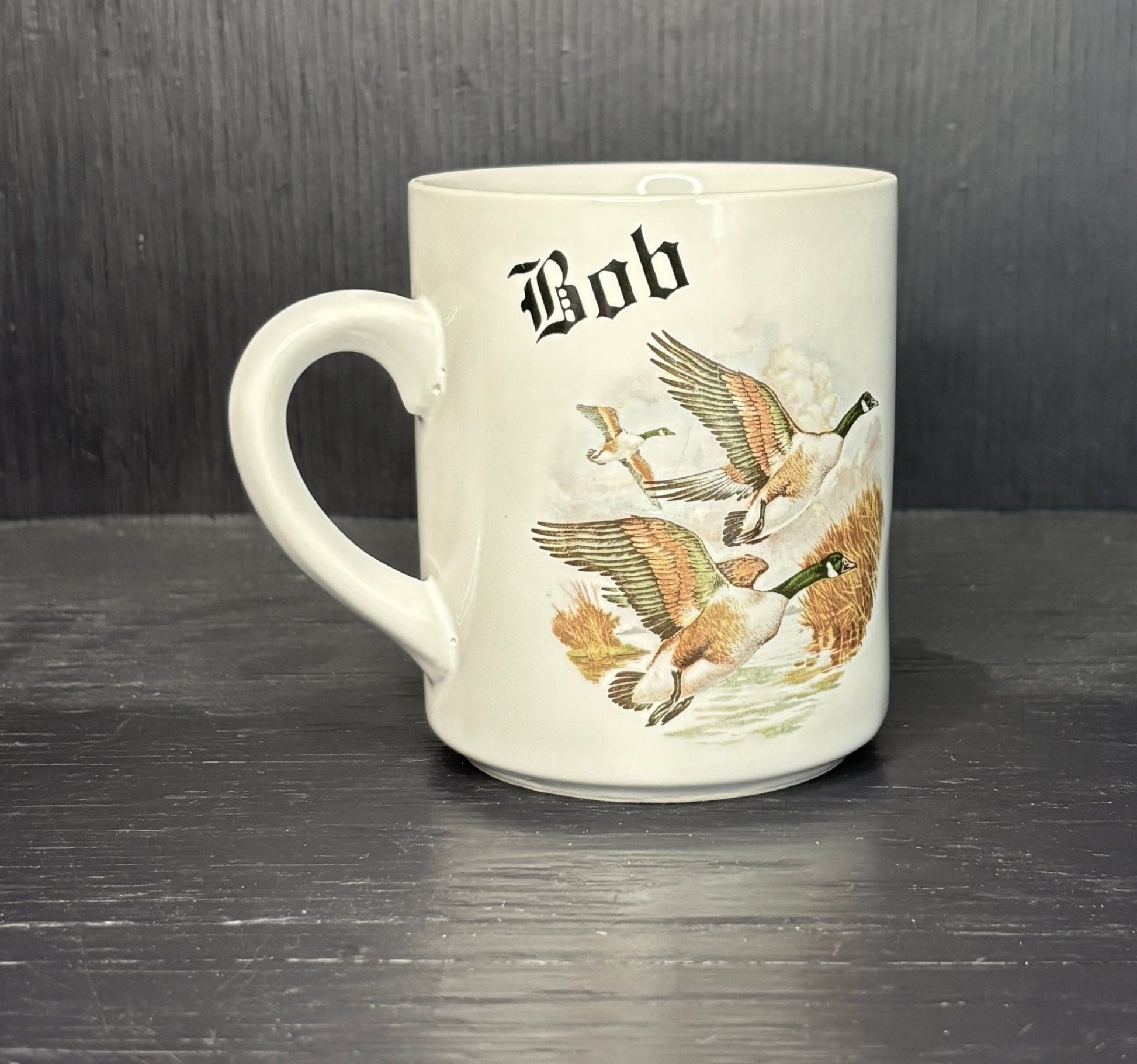 White mug with goose illustrations and 'Bob' text on a dark surface