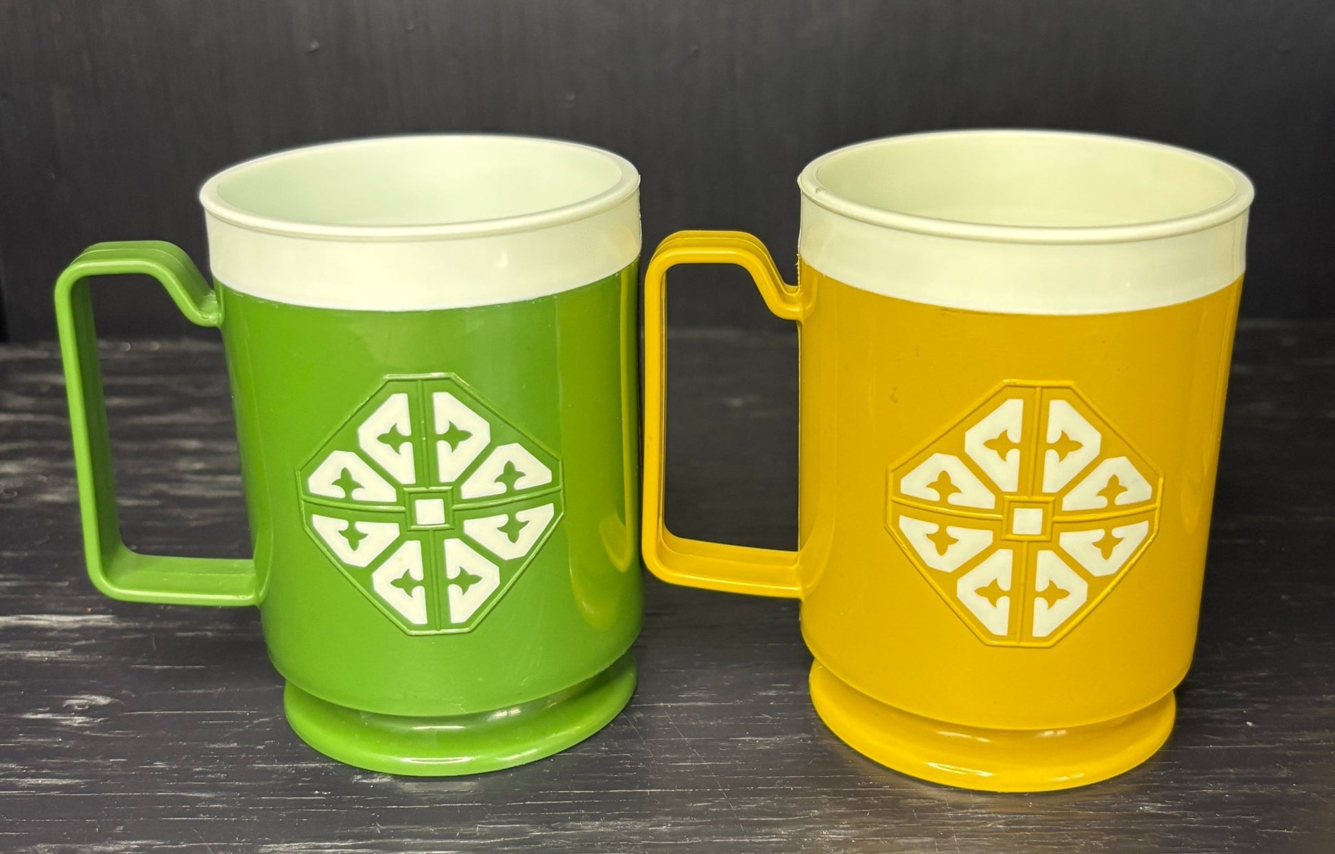 Two mugs, one green and one yellow, with a geometric design on a dark surface.