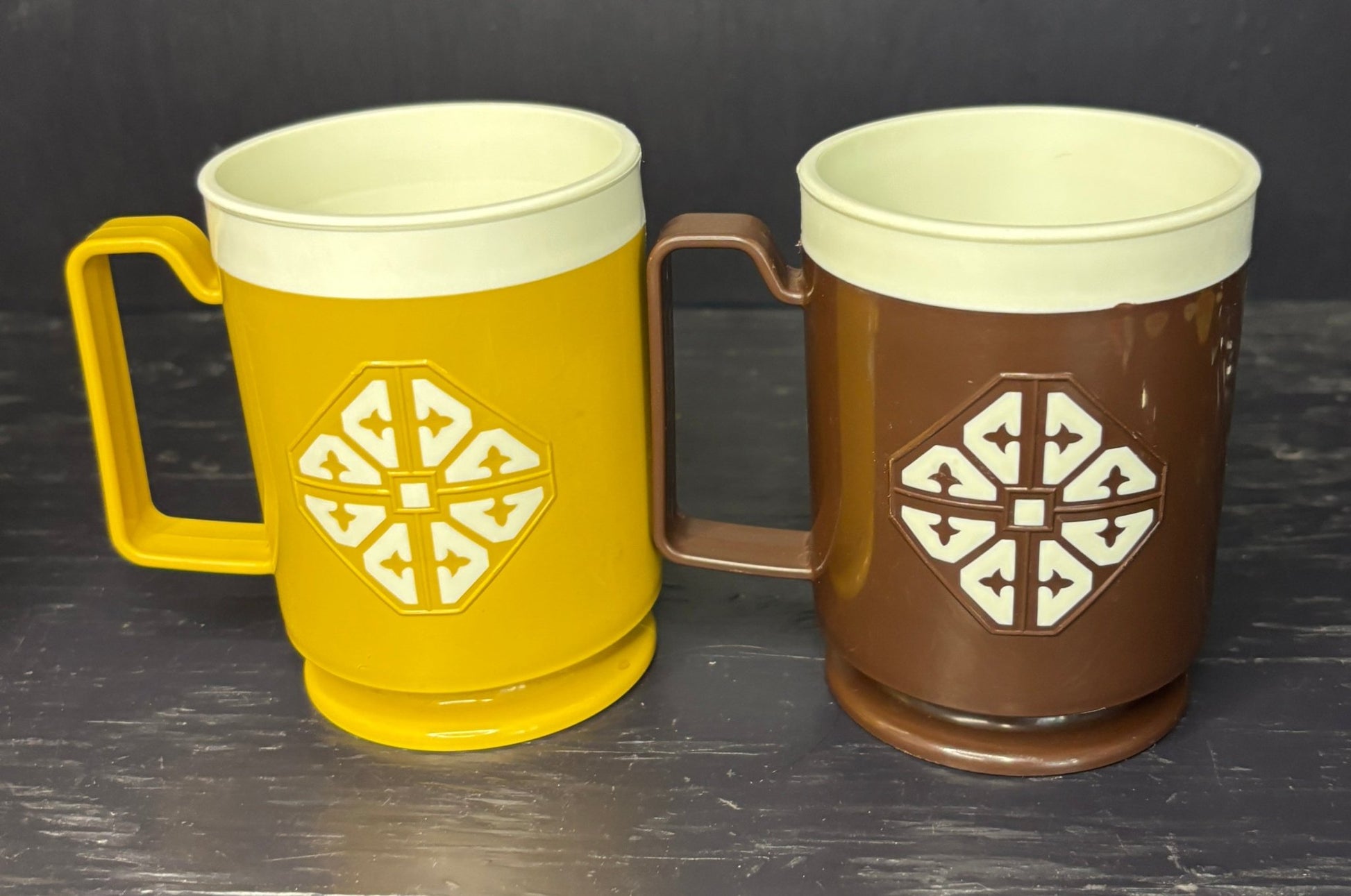 Two mugs, one yellow and one brown, with a geometric design on a dark background.