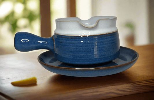 Blue ceramic teapot with lid on a matching saucer on a wooden surface.