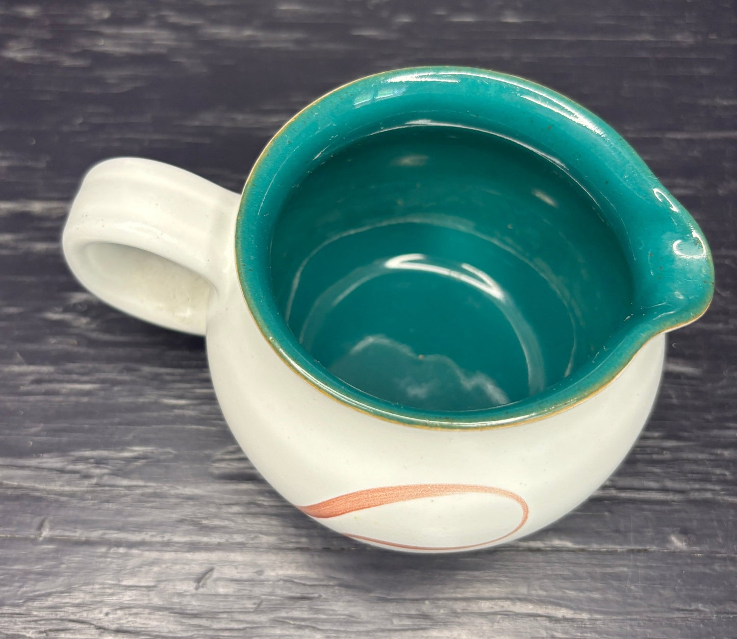Ceramic creamer with teal interior and white exterior on a dark wooden surface
