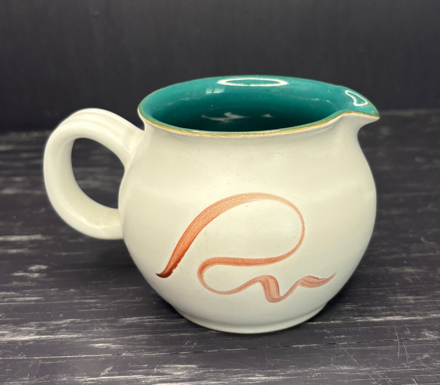 White ceramic pitcher with green interior and brown 'R' design on a dark surface