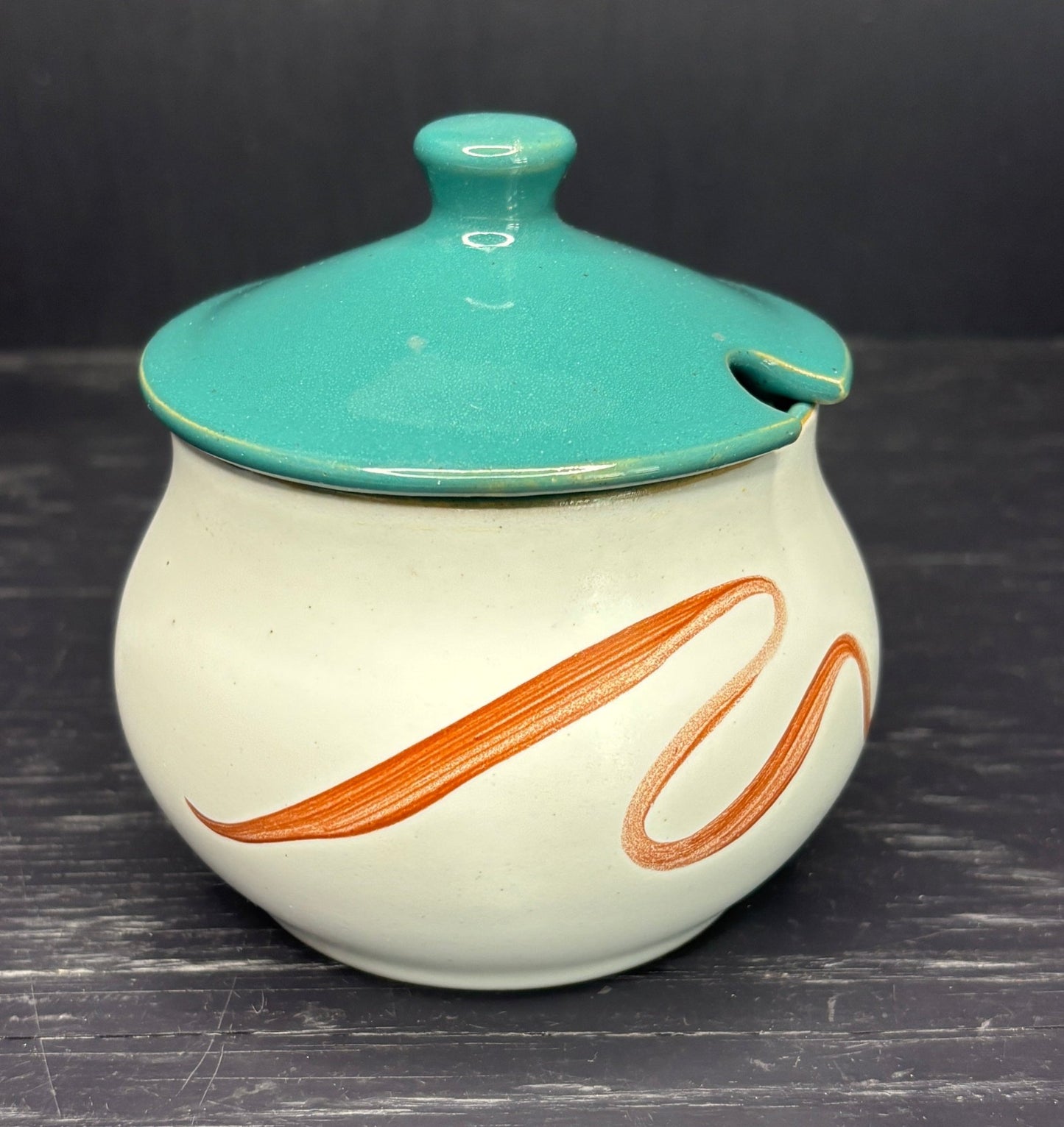 Ceramic jar with teal lid and orange design on a dark surface