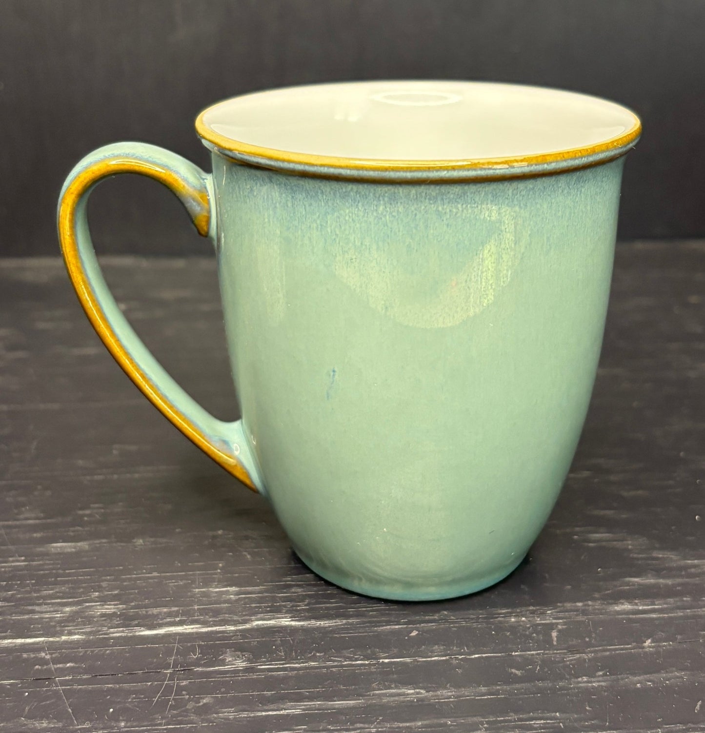 Green ceramic mug with gold rim and handle on a dark wooden surface