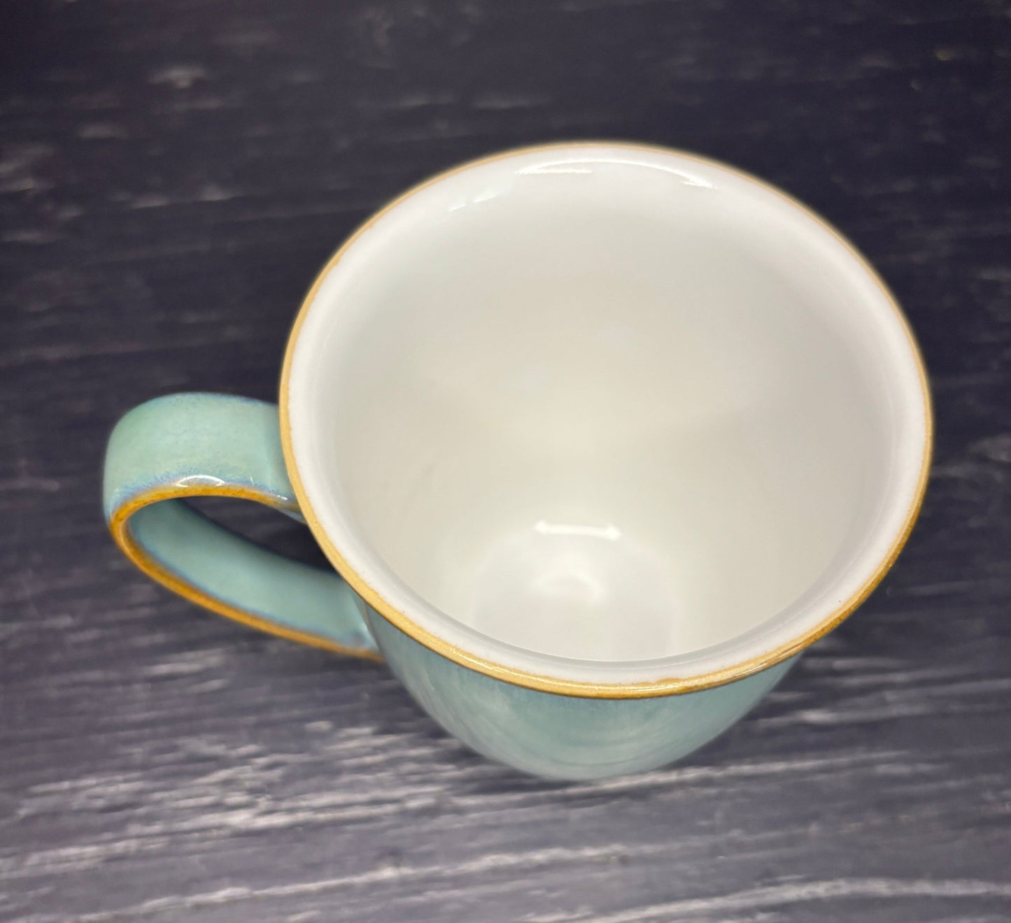 Light blue ceramic mug with gold rim on a dark textured surface