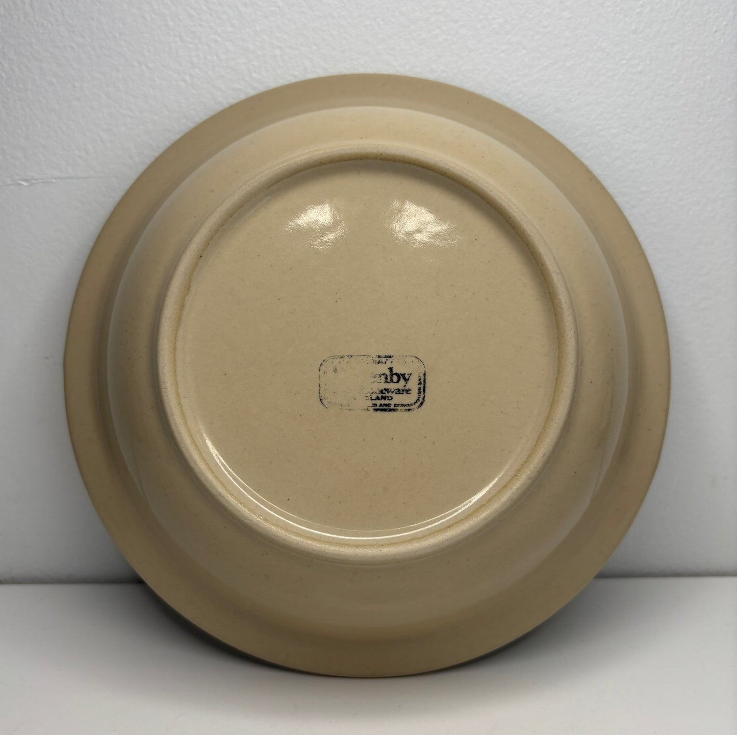 Beige ceramic plate with a visible brand logo on a white background