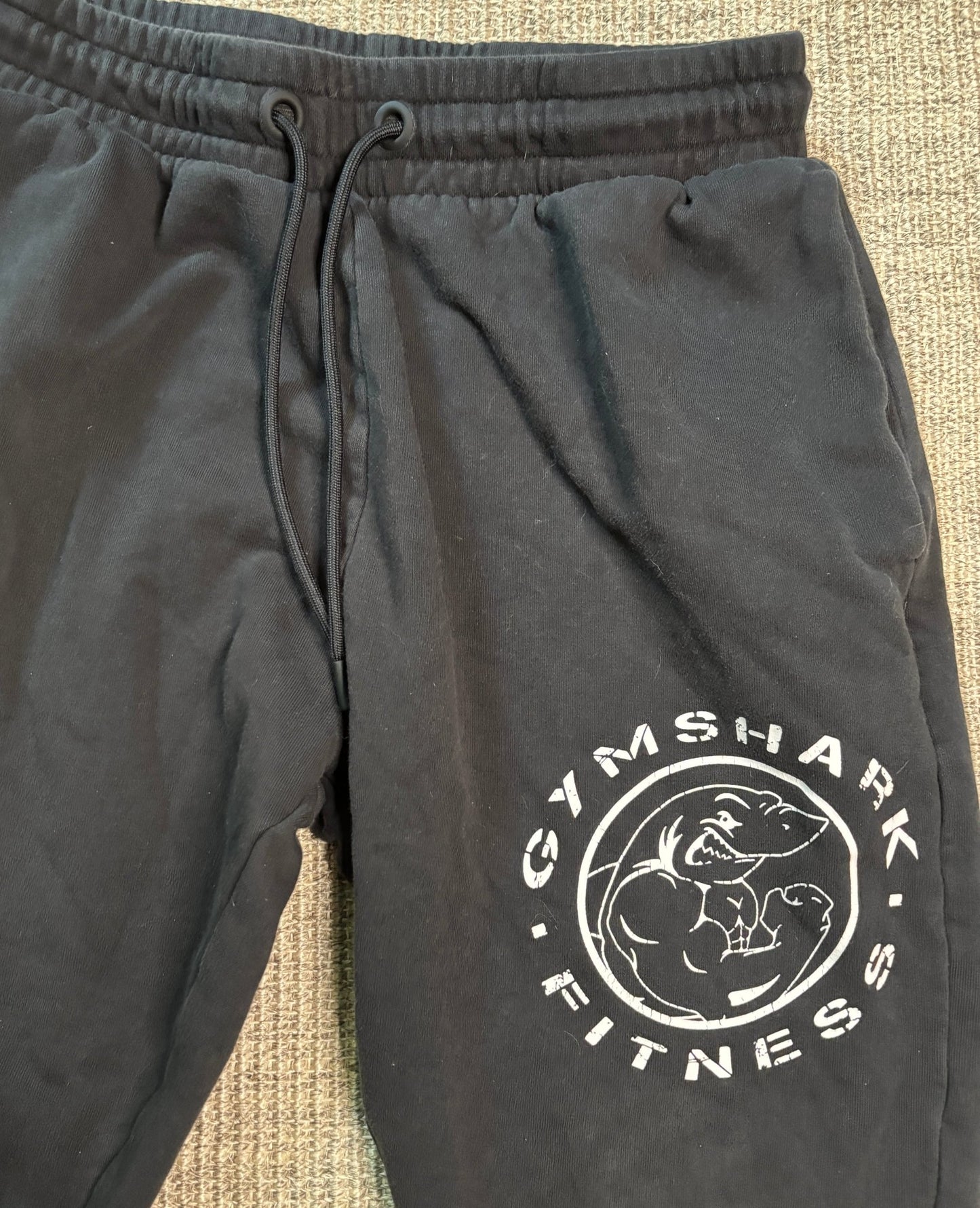 Black sweatpants with Gymshark Fitness logo on a textured surface