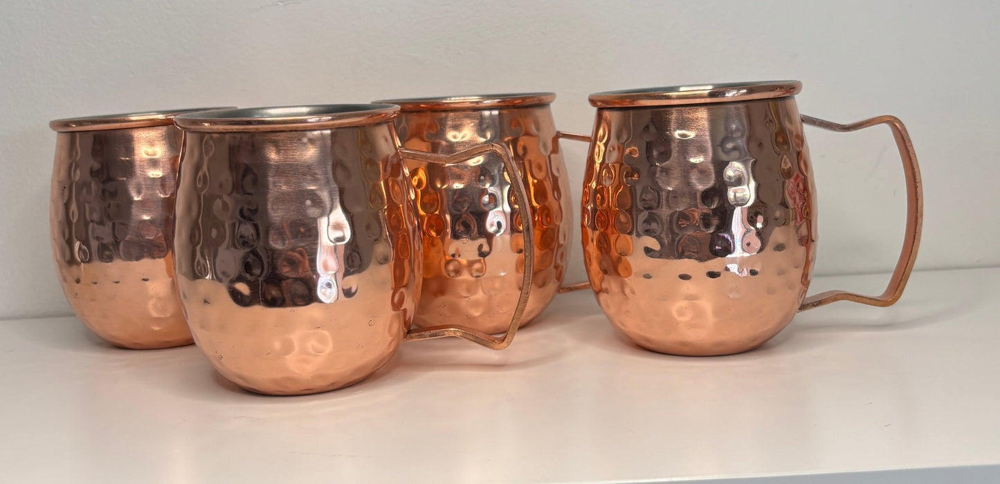 Set of four copper mugs with handles on a white surface