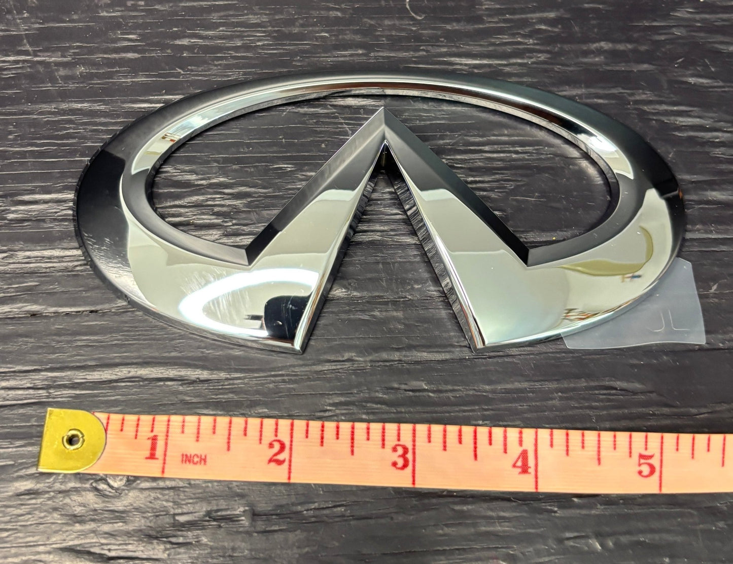 Chrome infiniti car emblem on a wooden surface with a ruler for scale.