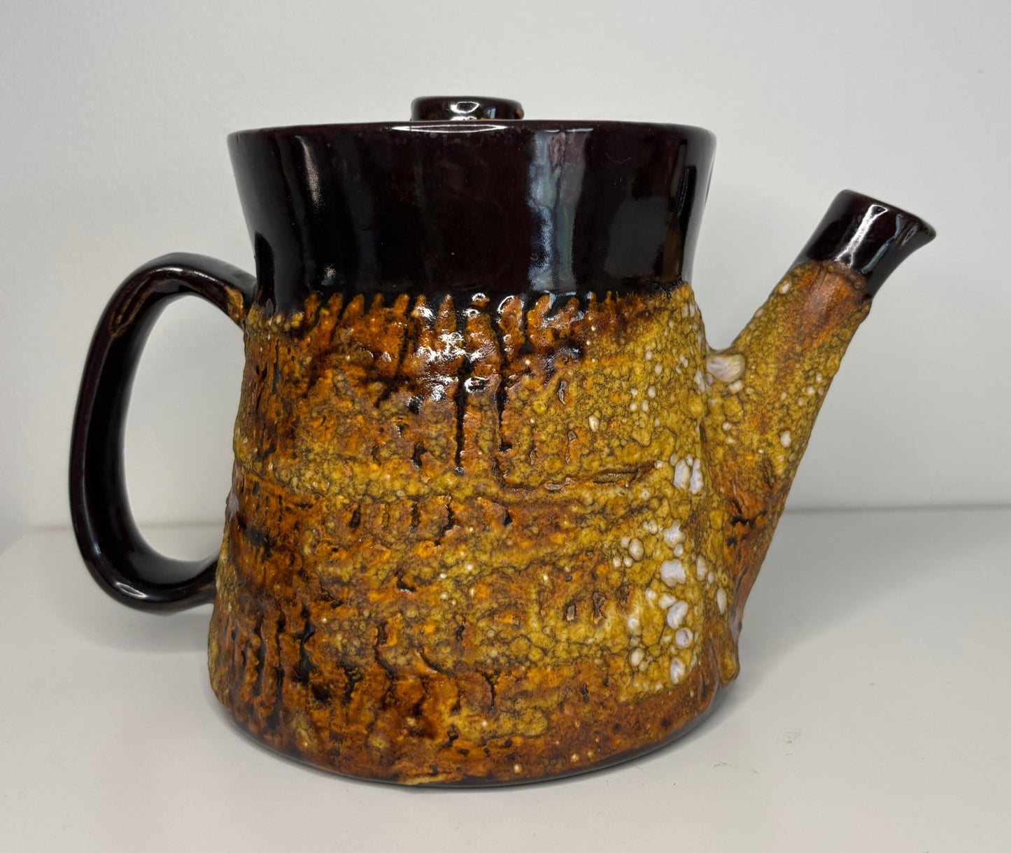 Ceramic teapot with textured brown body and black lid and handle on a white background