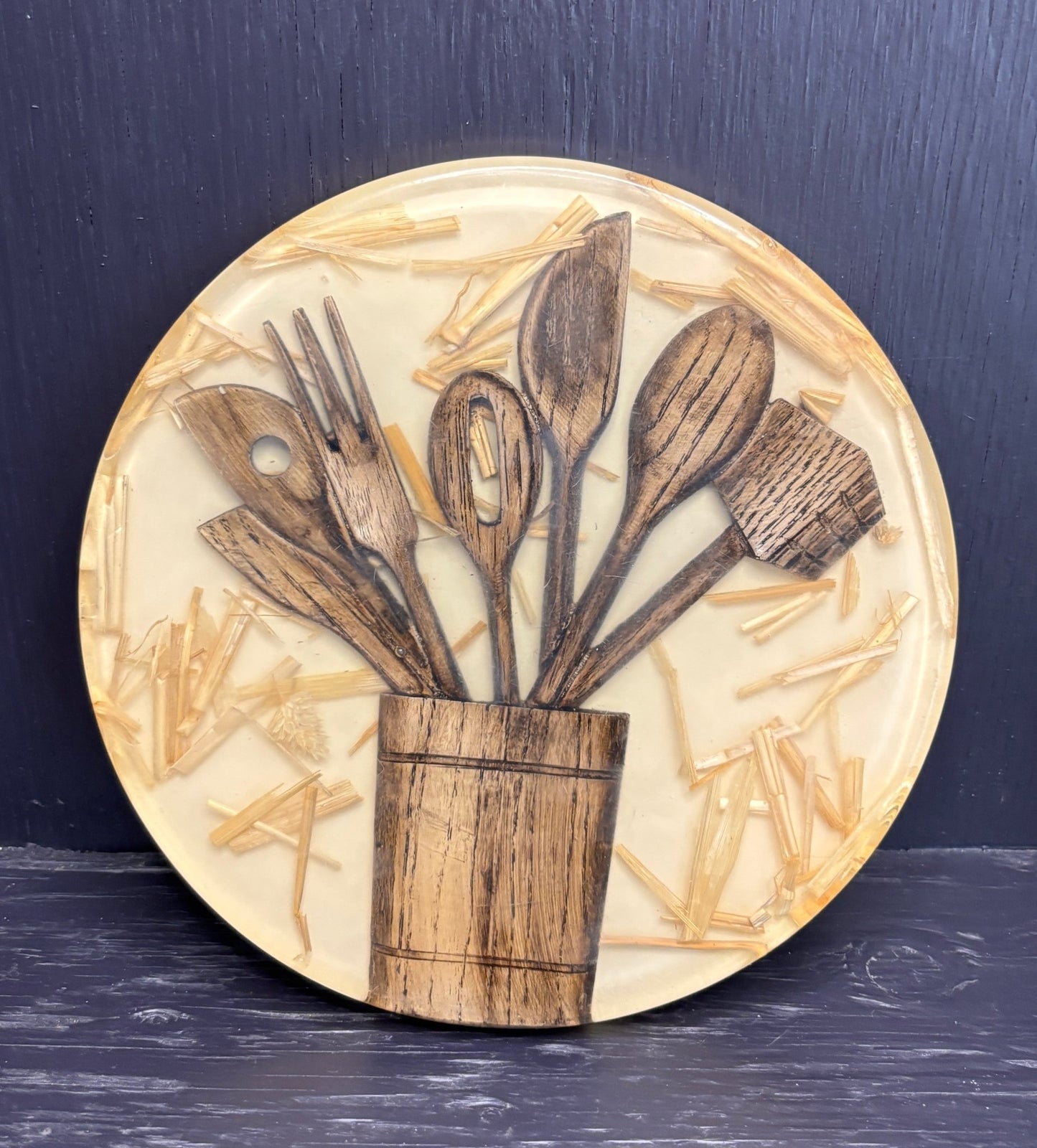 Round decorative pot stand with wooden cutlery design on a dark background
