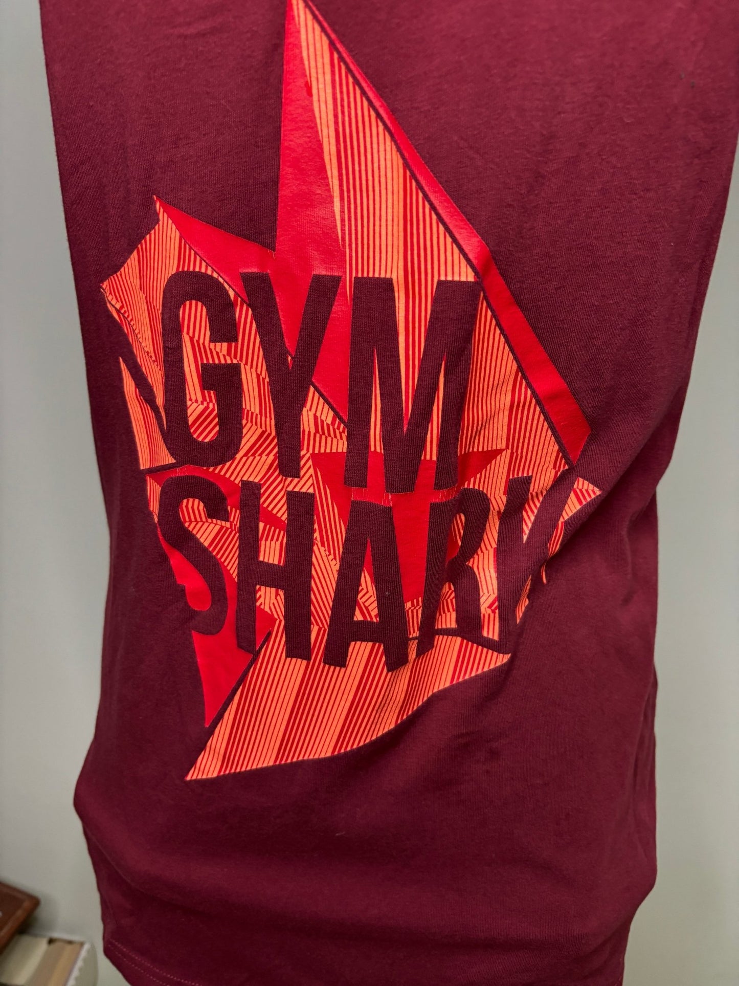 Maroon t-shirt with red and black 'Gym Shred' logo on a white surface