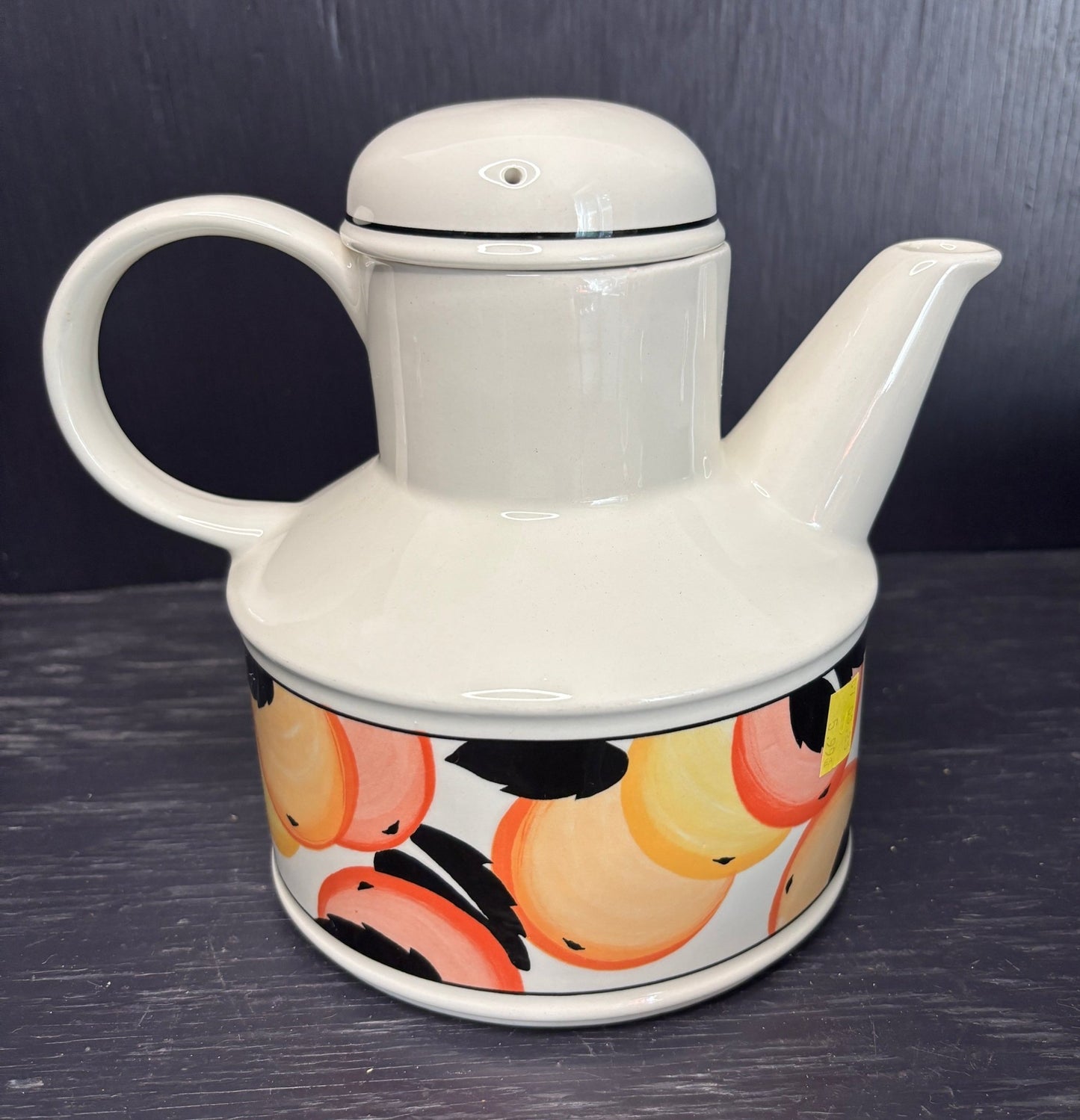 White teapot with a colorful fruit pattern on a dark surface