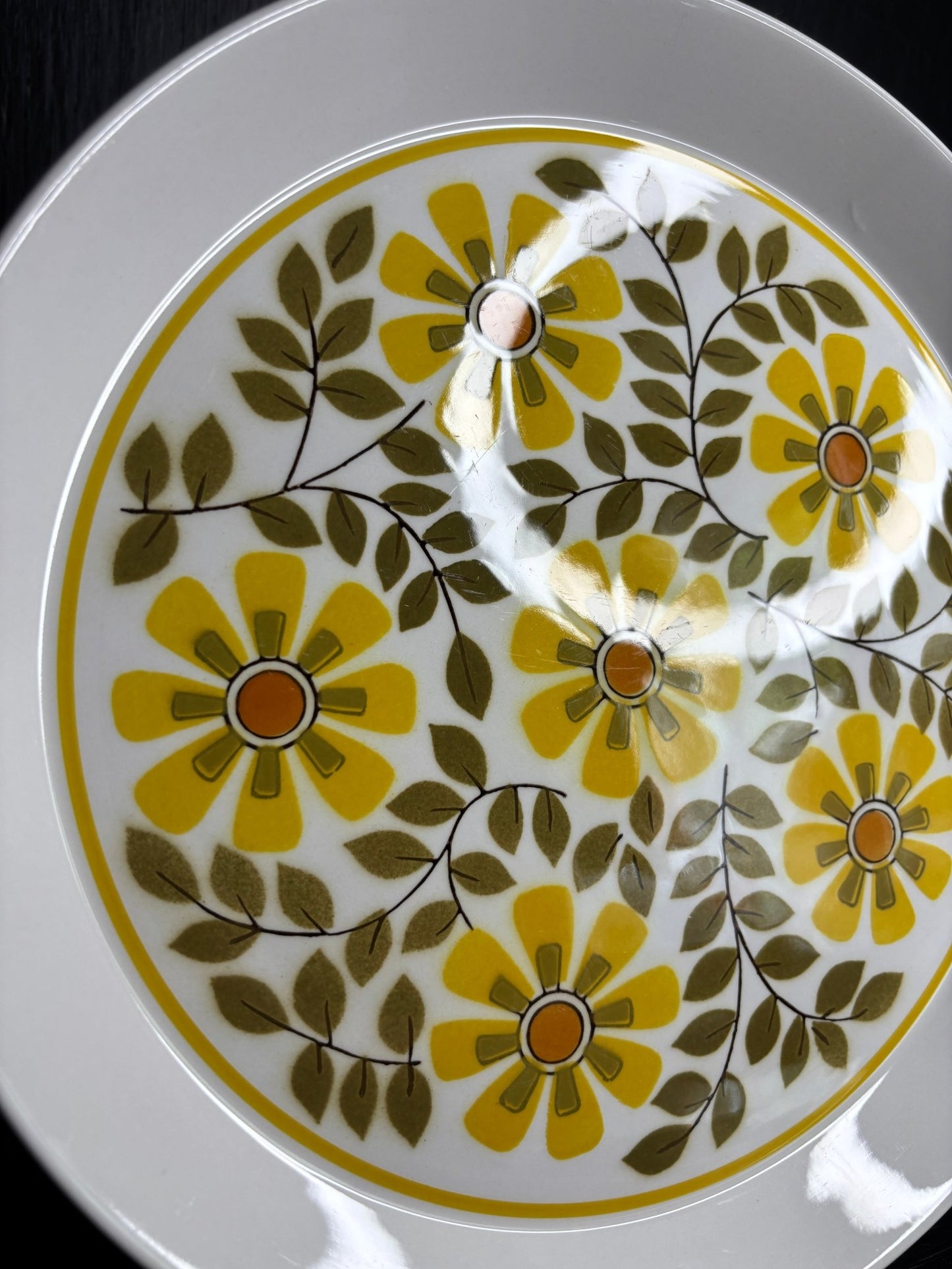 Decorative plate with yellow flowers and green leaves on a white background