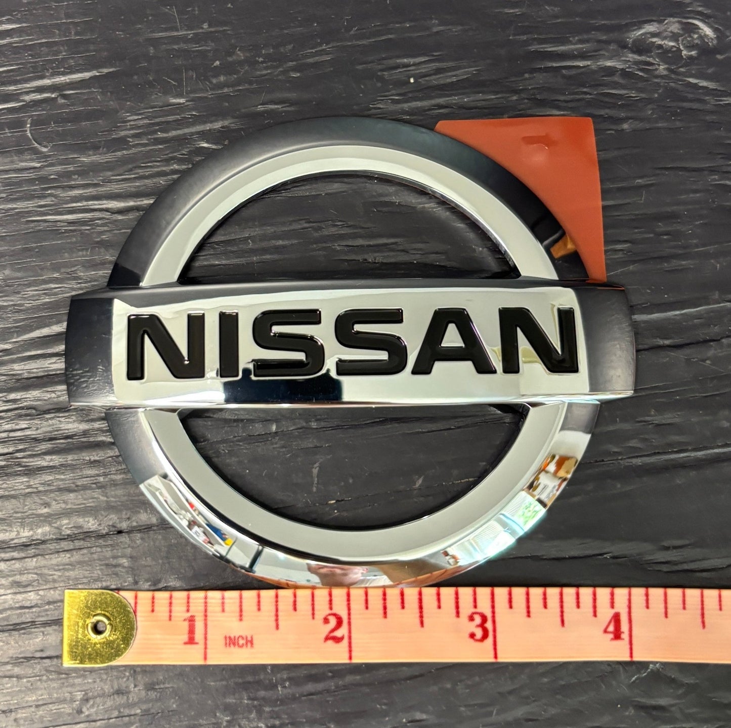 Nissan logo on a dark surface with a ruler for scale