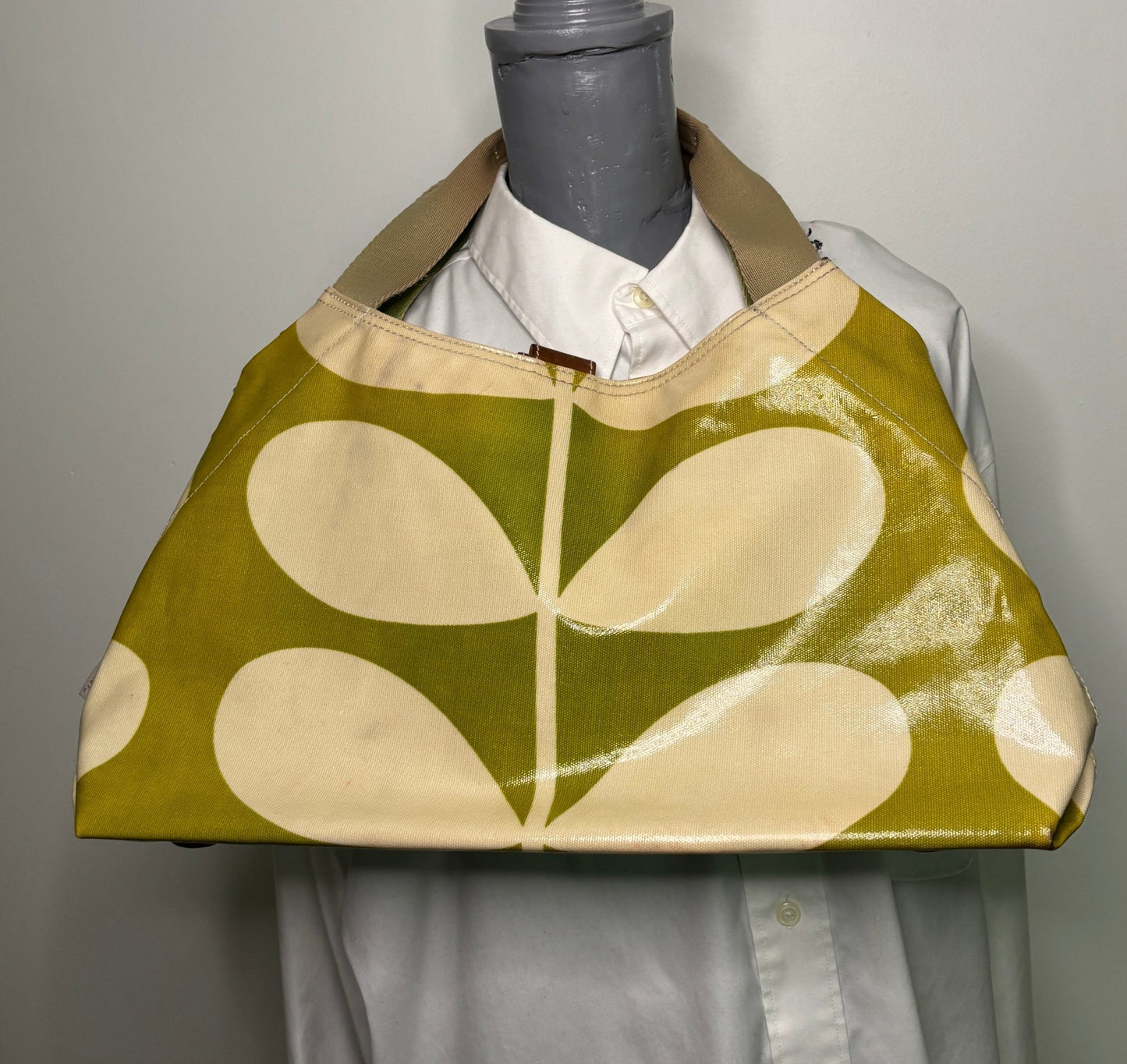 Green and beige patterned bag on a mannequin with a white shirt underneath.