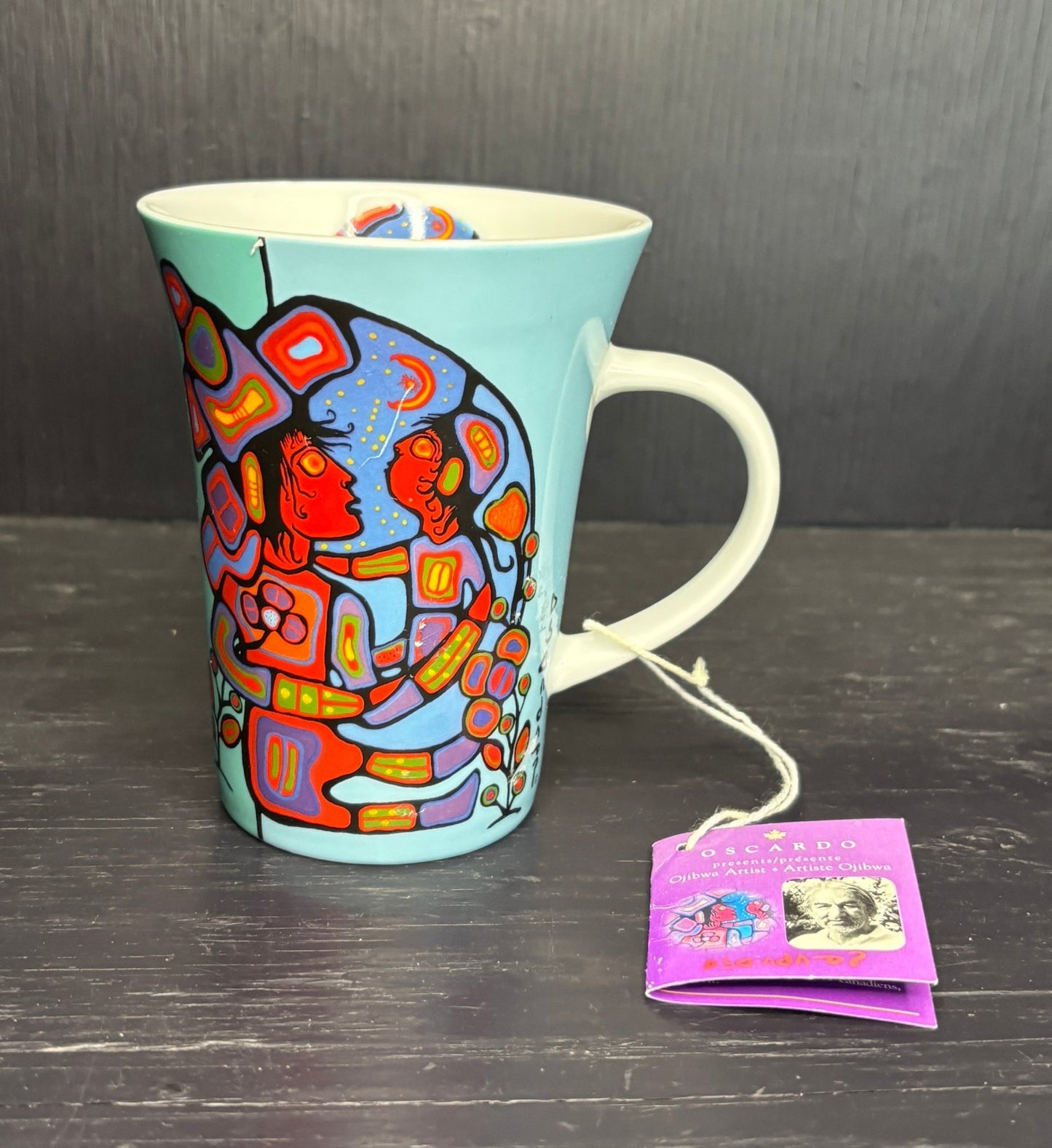 Colorful mug with artistic design on a dark surface, accompanied by a tea bag tag.
