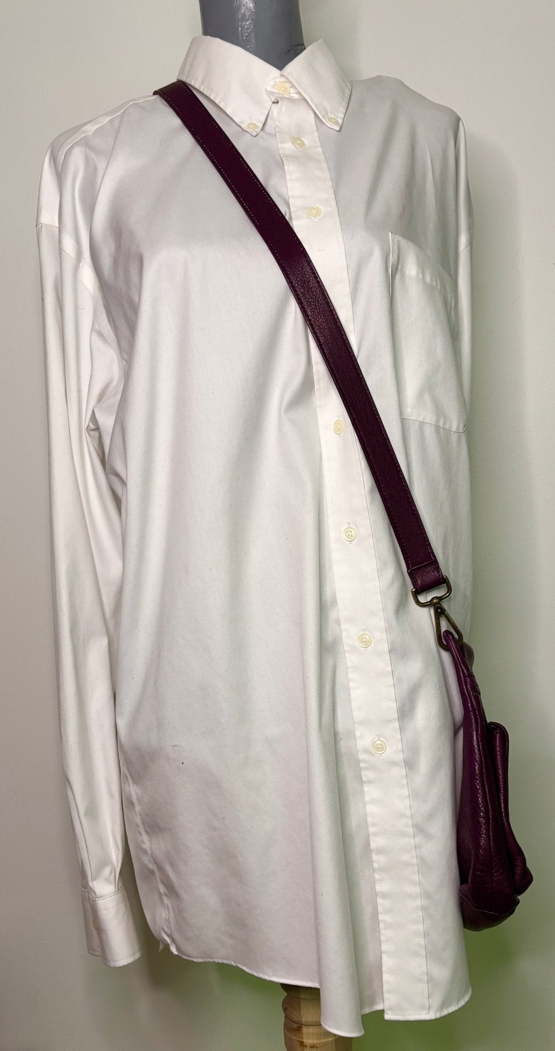 White shirt on a mannequin with a purple strap and bag against a plain background