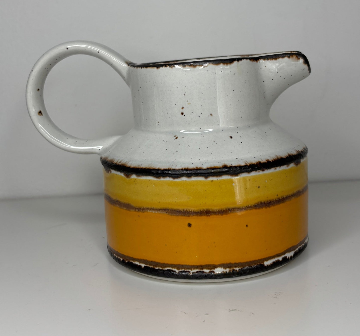 Ceramic pitcher with white top and yellow bottom on a plain background