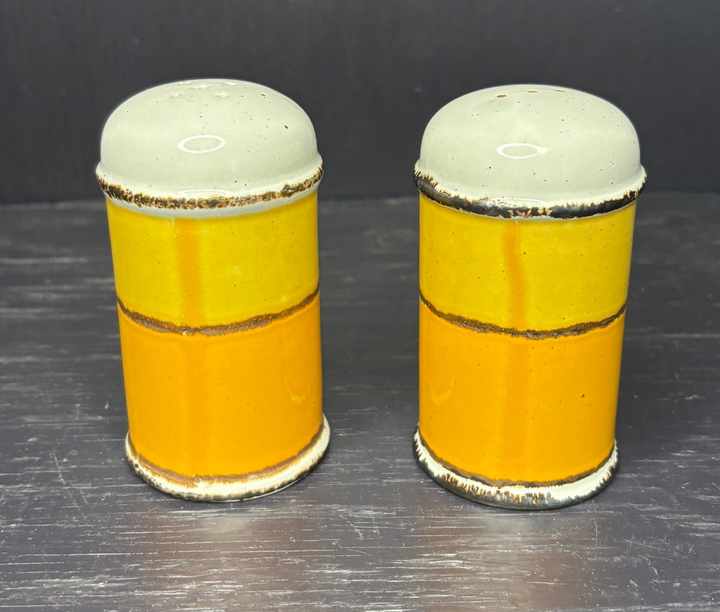 Two ceramic salt and pepper shakers with yellow bodies and white tops on a dark surface.