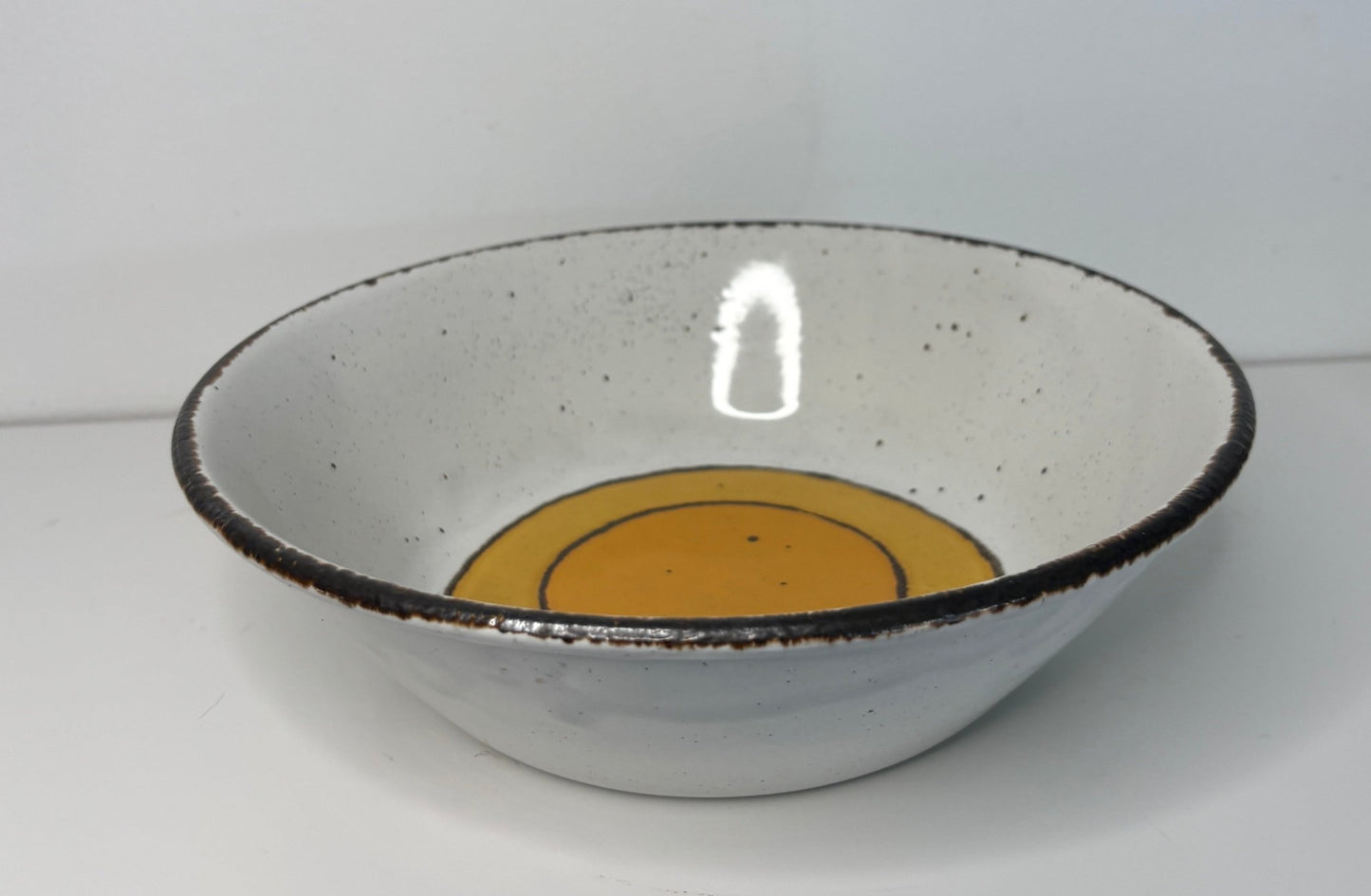 Ceramic bowl with a black rim and orange center on a white background