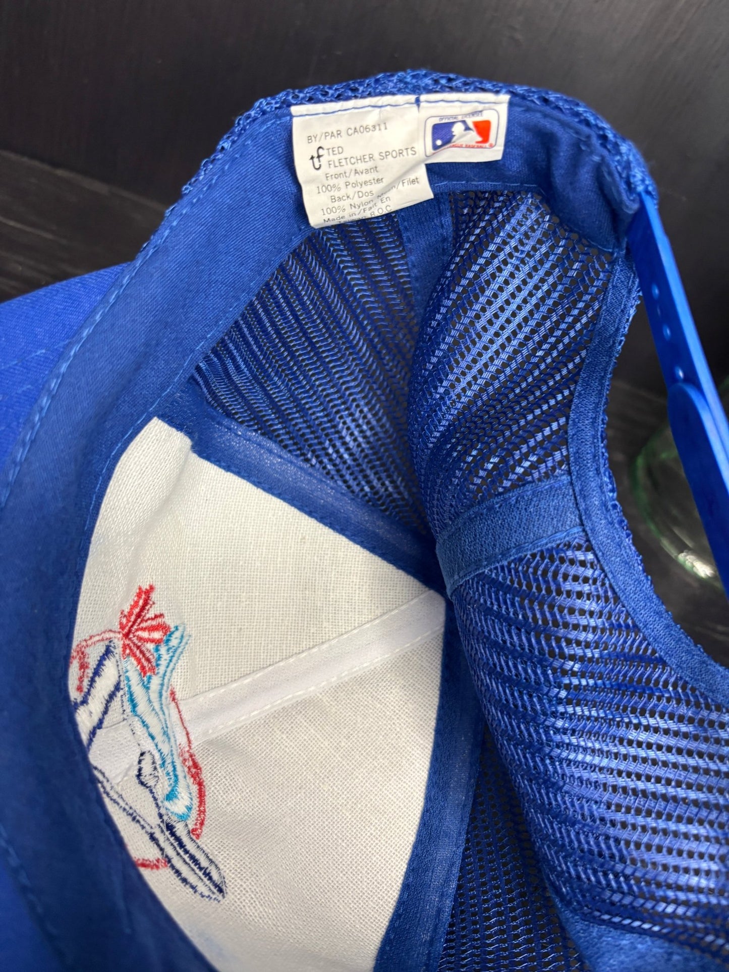 Close-up of a blue baseball cap with mesh back and embroidered logo on the visor.