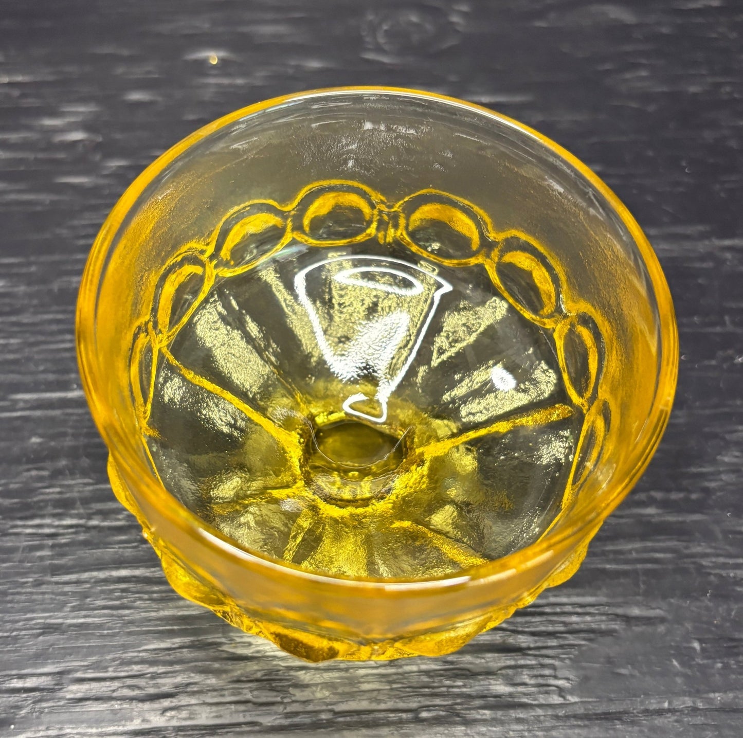Yellow glass bowl with decorative patterns on a dark wooden surface