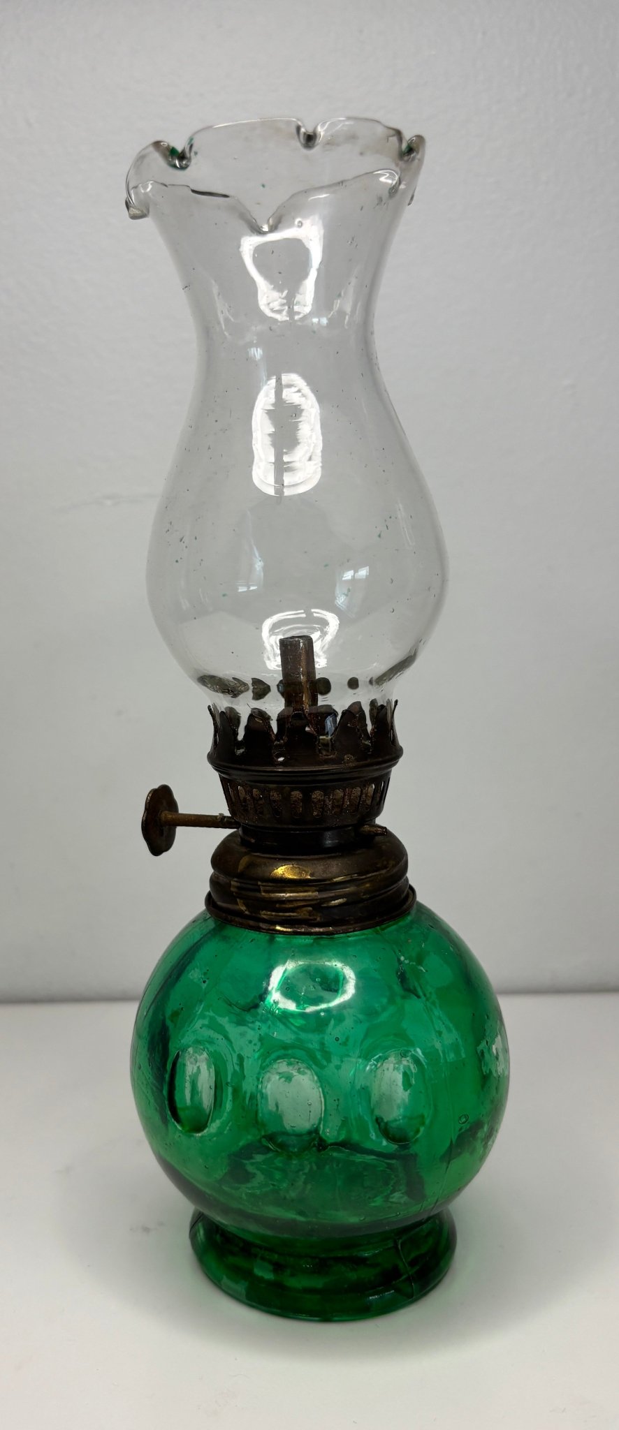 Vintage oil lamp with green base and clear glass chimney on a white background