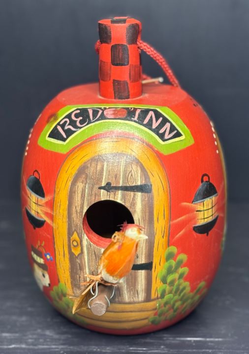 Decorative birdhouse with a red exterior and wooden door, featuring a bird illustration on a dark background.