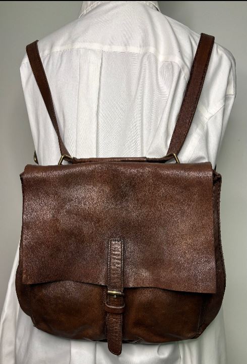 Brown leather backpack worn by a person in a white shirt against a neutral background