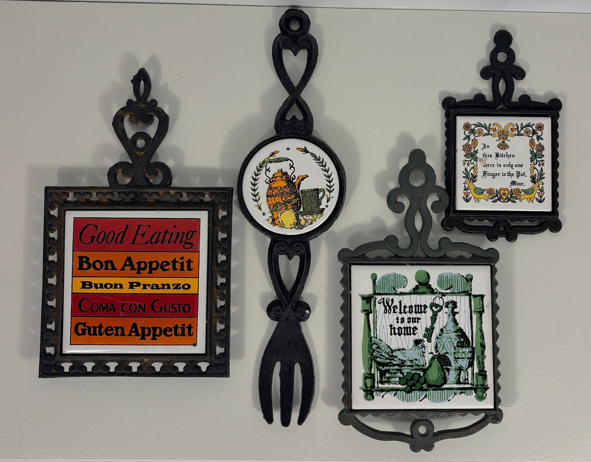 A set of five decorative wall-mounted plates and signs in black metal frames, including food-themed sayings like 'Good Eating Bon Appetit' and 'Welcome to our home', displayed against a light gray wall.