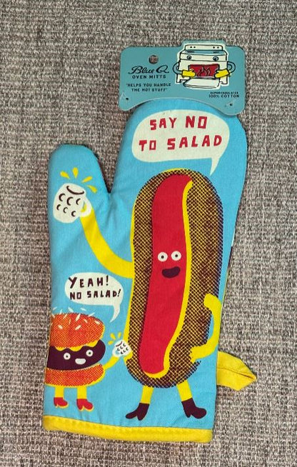 Oven mitt with cartoon hot dog character and humorous text on a gray surface