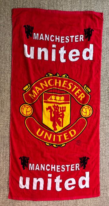 Red Manchester United towel with logo and text on a textured surface