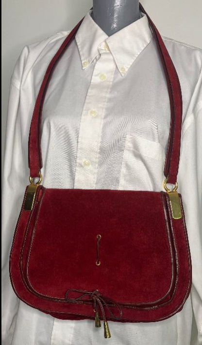 Red suede handbag with gold accents on a mannequin wearing a white shirt.