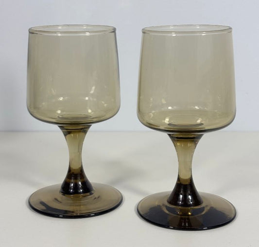 A pair of vintage amber-tinted glass goblets with bulbous bodies and flared bases, photographed against a neutral light gray background.
