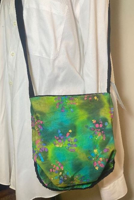 Colorful handbag with floral pattern held by a person wearing a white shirt.