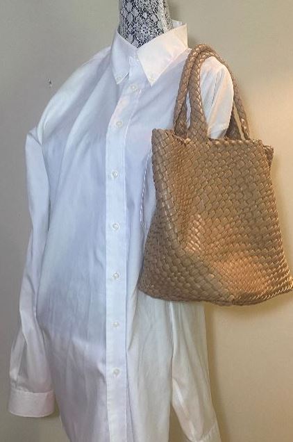 Mannequin wearing a white shirt with a woven beige handbag on a plain background