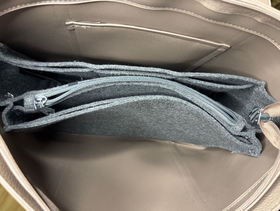 Open beige handbag with gray interior showing zippers and fabric texture.