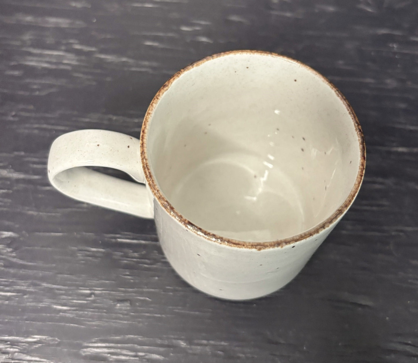 White ceramic mug with brown rim on a dark textured surface