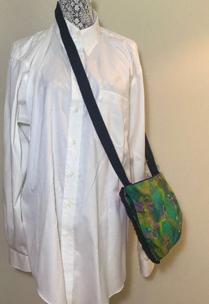 Mannequin wearing a white shirt with a green and black patterned bag over its shoulder against a plain background