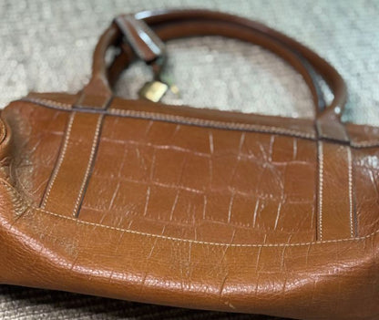 Brown leather handbag with visible wear on a textured surface