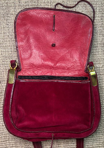 Red leather bag with gold zippers on a textured surface