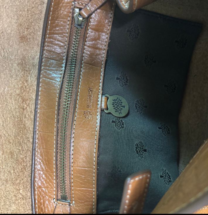 Close-up of a brown leather bag with a zipper and decorative interior lining.
