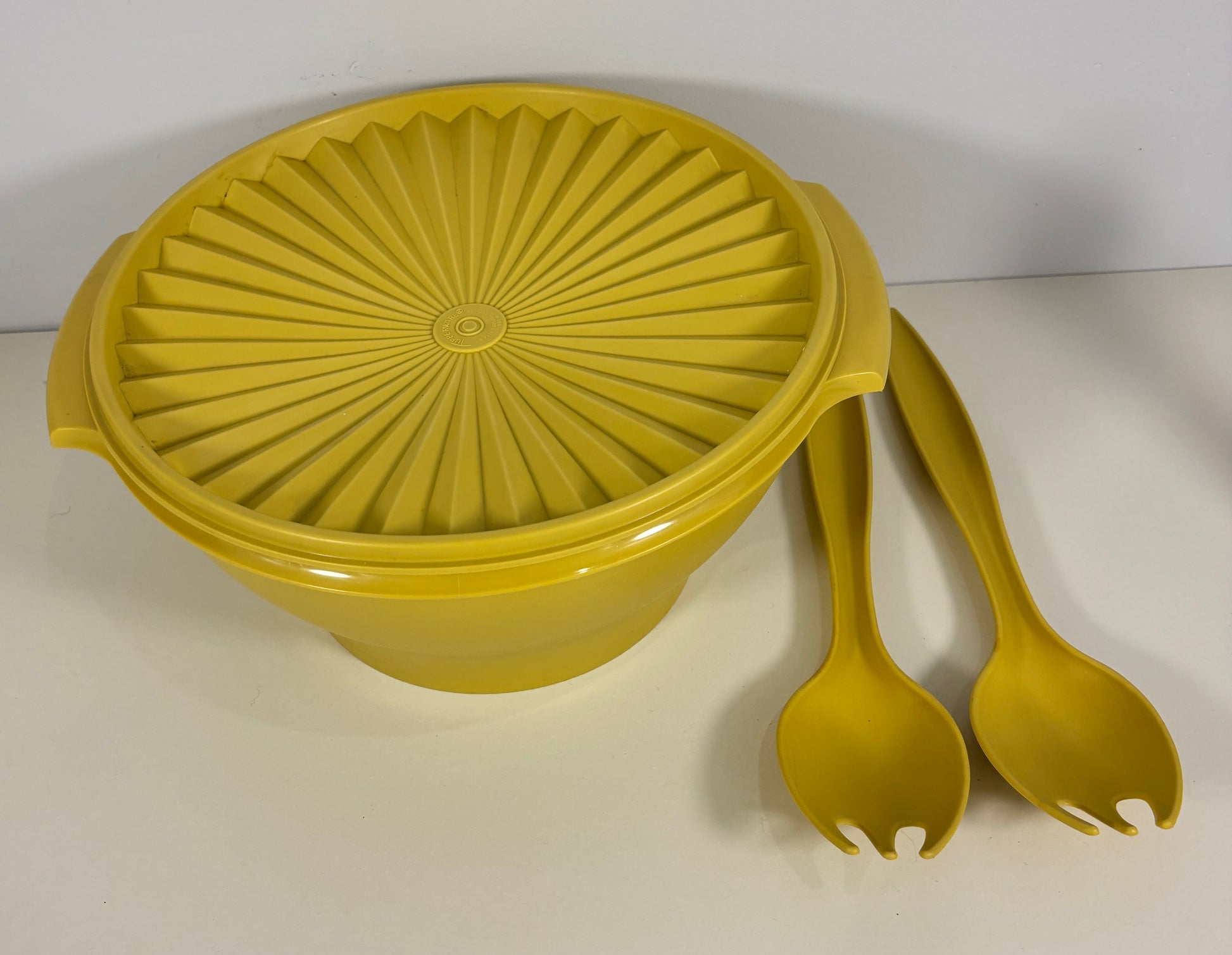 Yellow plastic salad spinner with two utensils on a white background
