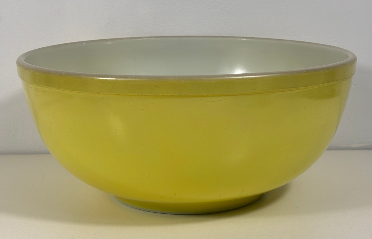 A round mixing bowl with a pale yellow exterior and a light gray interior, photographed against a plain off-white background.