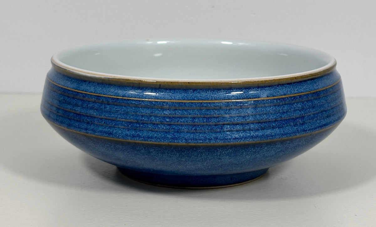 A ceramic bowl with a textured cobalt blue exterior featuring horizontal ridges and a contrasting light blue glazed interior, set against a plain light gray background.