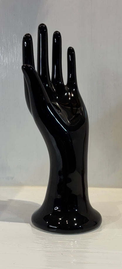 Black hand-shaped vase on a reflective surface with a light gray background