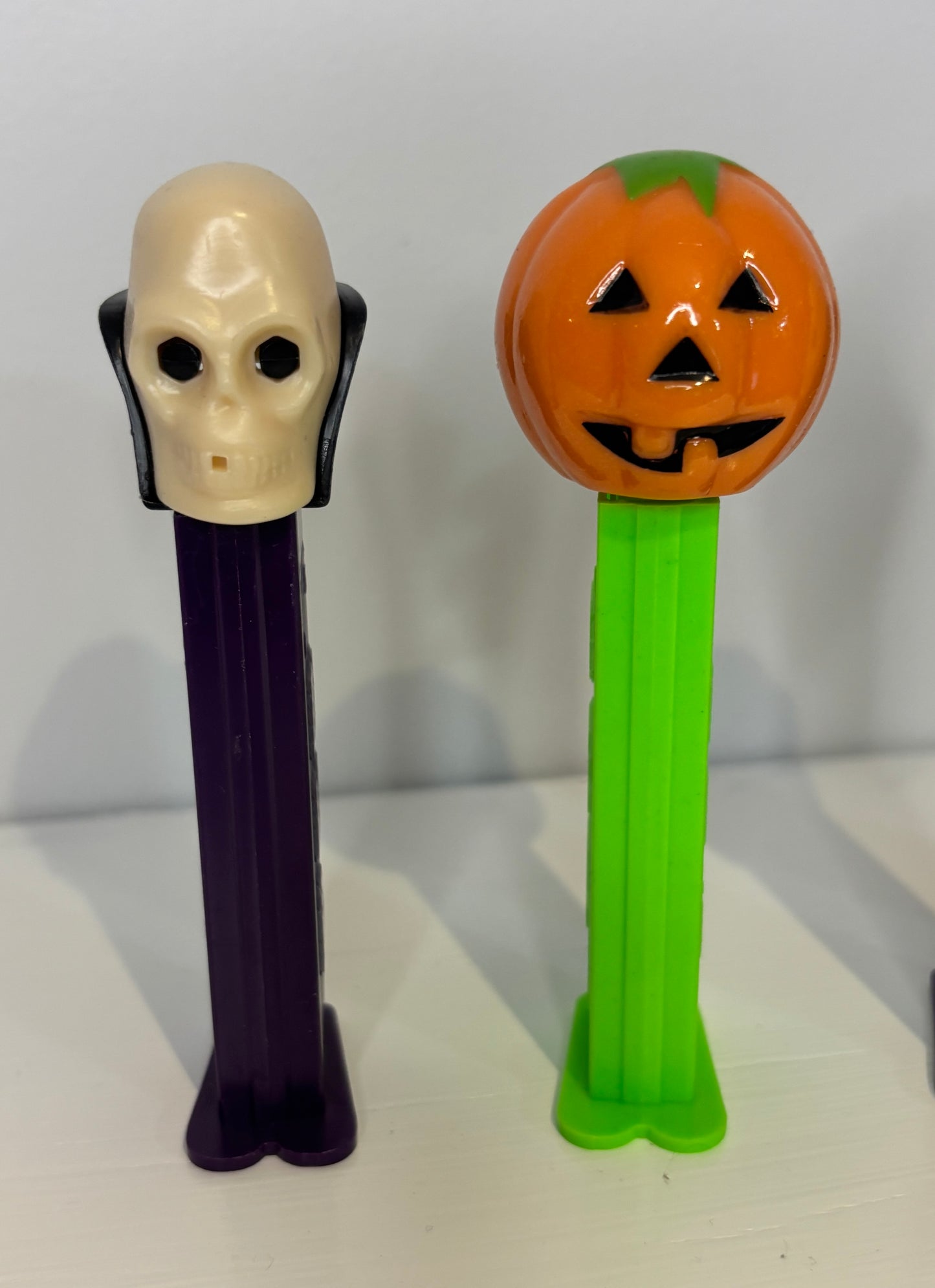 Two Halloween-themed PEZ dispensers, one with a ghost head and the other with a pumpkin design, on a white background.